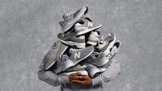 Model holding up several grey New Balance sneakers.